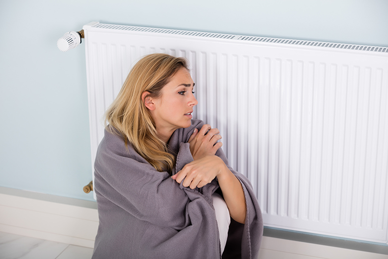 Young Cold Woman Wrapped In Blanket Sitting Near Central Heating System At Home